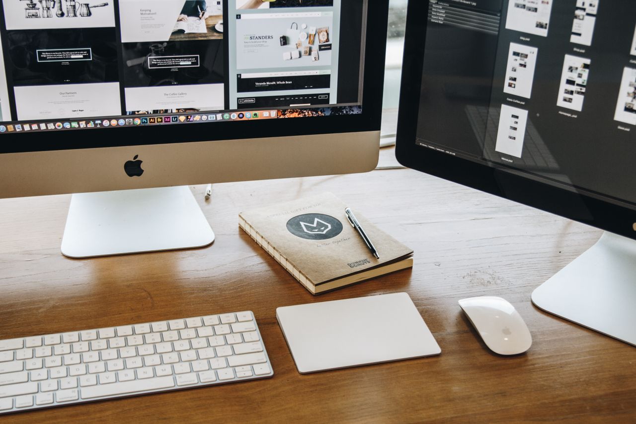 our-story A minimalist desk setup featuring dual monitors, keyboard, mouse, and notebook for productivity.